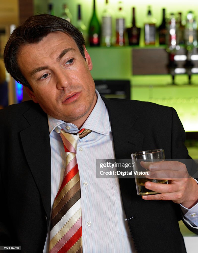 Drunk Businessman Standing by a Bar With a Whisky in His Hand