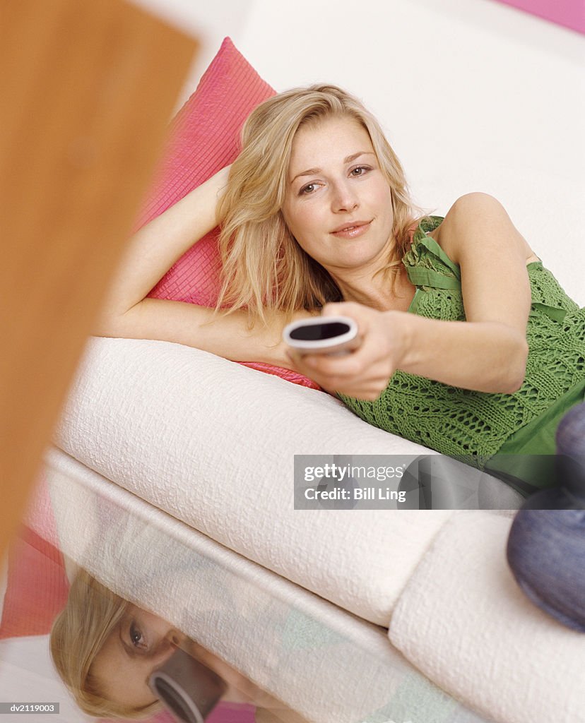 Woman Lying on a Sofa Watching Television and Using a Remote Control