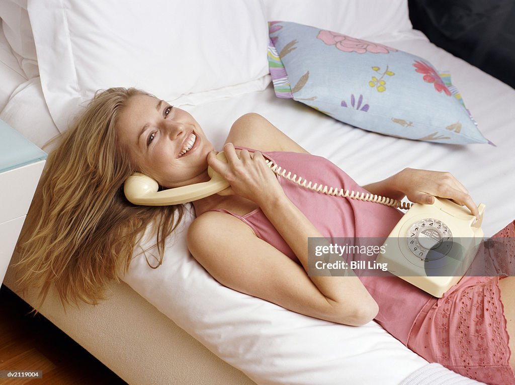 Woman Lying on a Bed Using a Telephone