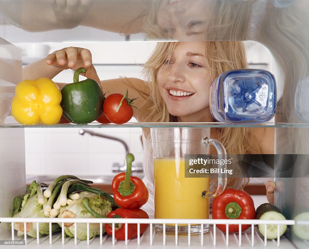 Woman Reaching for a Green Pepper in a Fridge