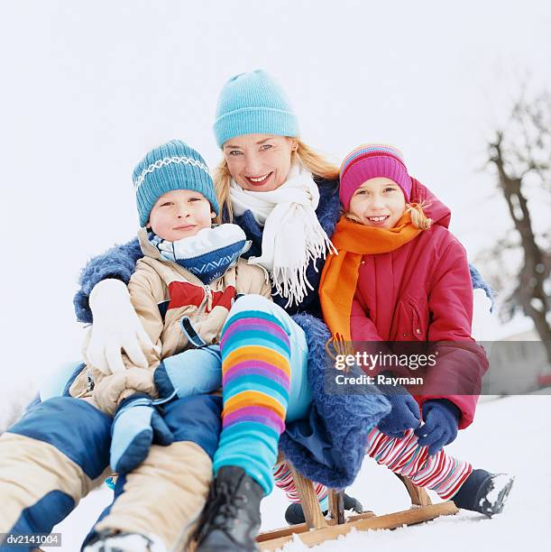 mother with two children sitting outdoors on a sled in the snow - boys wearing tights stock-fotos und bilder