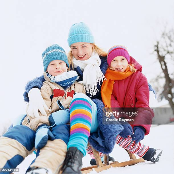 mother with two children sitting outdoors on a sled in the snow - boys wearing tights 個照片及圖片檔