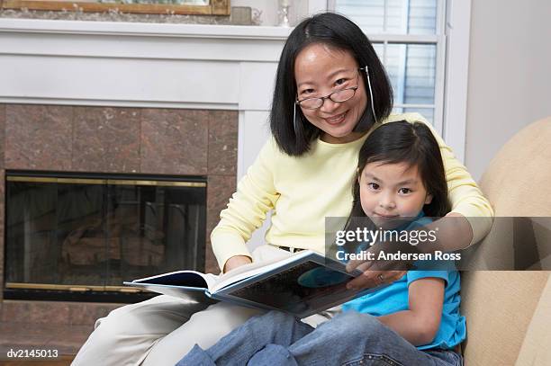 portrait of a woman sitting in a chair reading a book with her young daughter - andersen ross stockfoto's en -beelden