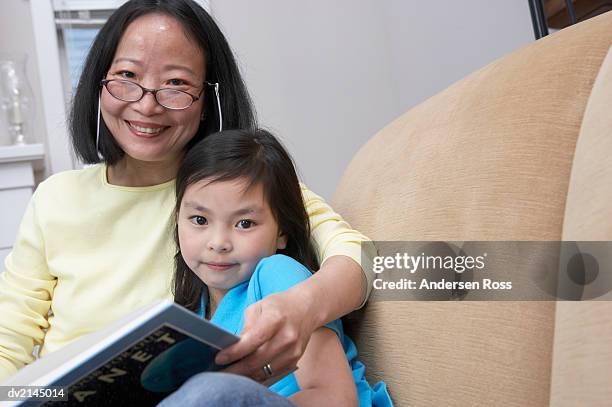 portrait of a woman sitting in a chair reading a book with her young daughter - andersen ross stock pictures, royalty-free photos & images