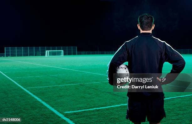 man holding a football and looking out over an empty football pitch - tracksuit jacket stock-fotos und bilder