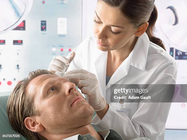 man receiving plastic surgery treatment in his forehead with a syringe - surgeon holding needle stock-fotos und bilder