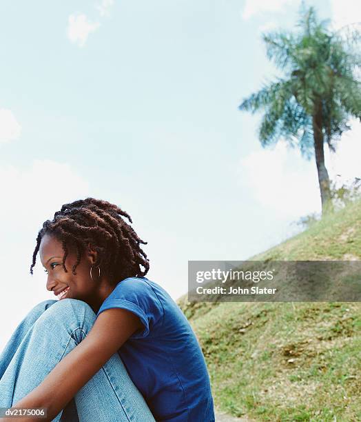 young woman sits on a hill, looking ahead and smiling - ahead stock pictures, royalty-free photos & images