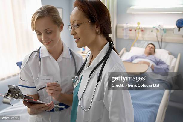 female nurse and doctor stand by a hospital bed discussing the patient's charts - contact avec les patients photos et images de collection