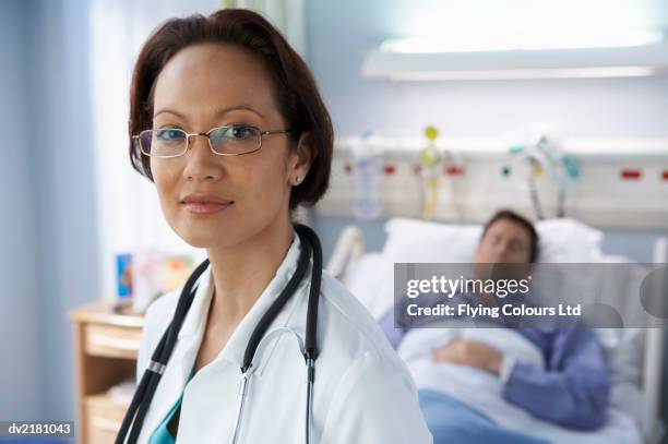 portrait of a female doctor with a male patient lying in bed in the background - rapporto medico paziente foto e immagini stock