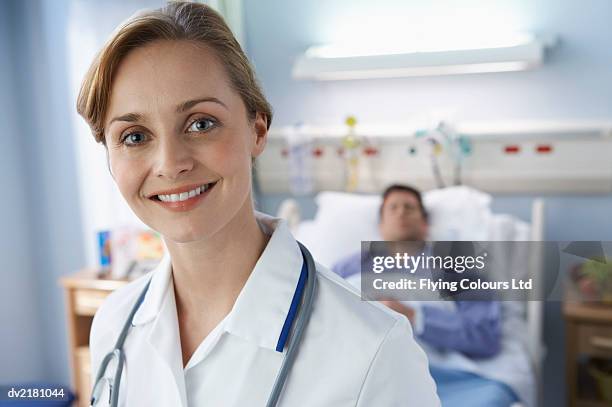 portrait of a female doctor with a male patient lying in bed in the background - rapporto medico paziente foto e immagini stock