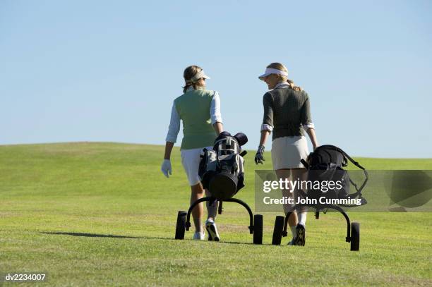 rear view of two woman walking on a putting green with golf equipment in golf bags - golftasche ziehen stock-fotos und bilder