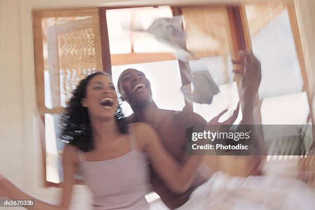 couple sitting in bed tossing money into air - air date stockfoto's en -beelden