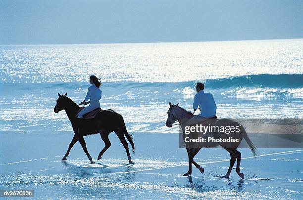 couple riding horses on beach - recreational horseback riding stock pictures, royalty-free photos & images