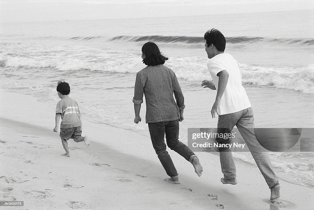 Mother and father chasing young son on beach