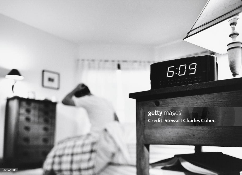 Alarm clock with man getting out of bed in background