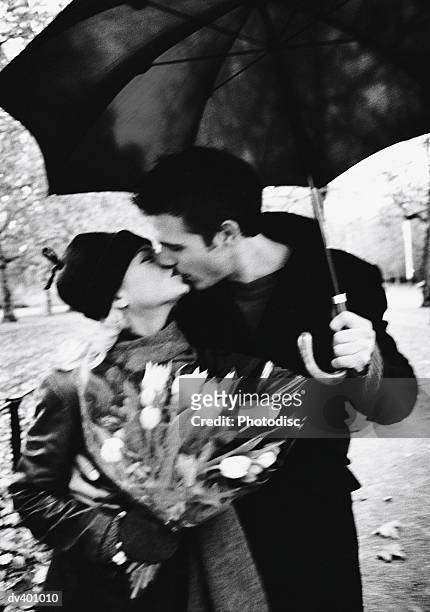 couple kissing under umbrella in park - couples kissing shower photos et images de collection