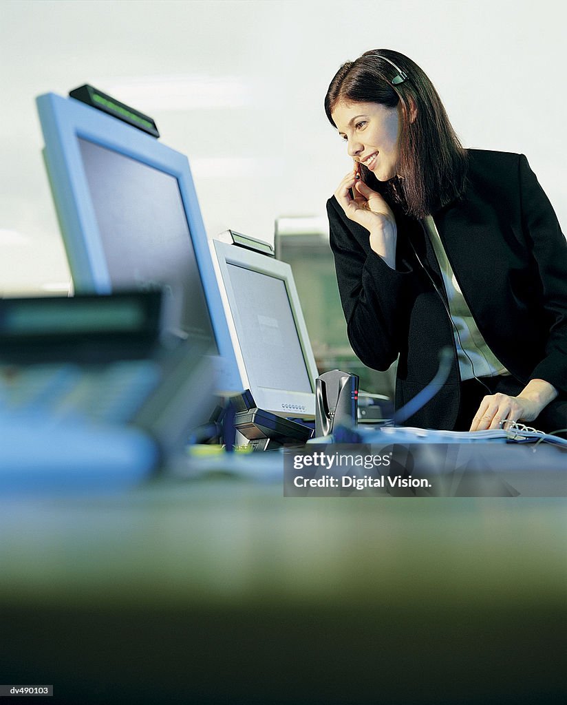 Businesswoman Wearing a Headset and Sitting on a Desk