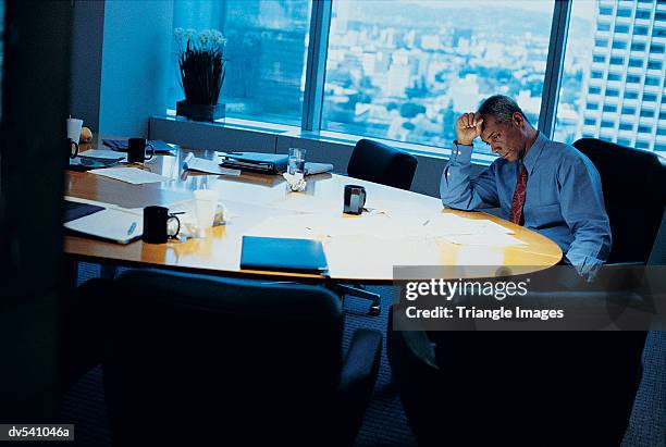 pensive businessman sitting at a boardroom table on his own - grené prononcé photos et images de collection