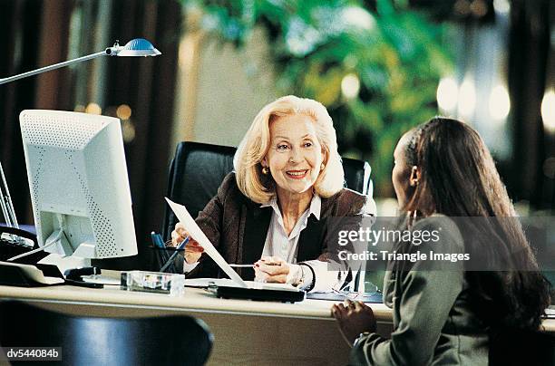 senior businesswoman giving an interview at her desk - grano fuerte fotografías e imágenes de stock