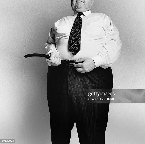 fat businessman fastening his belt - tighten stock pictures, royalty-free photos & images