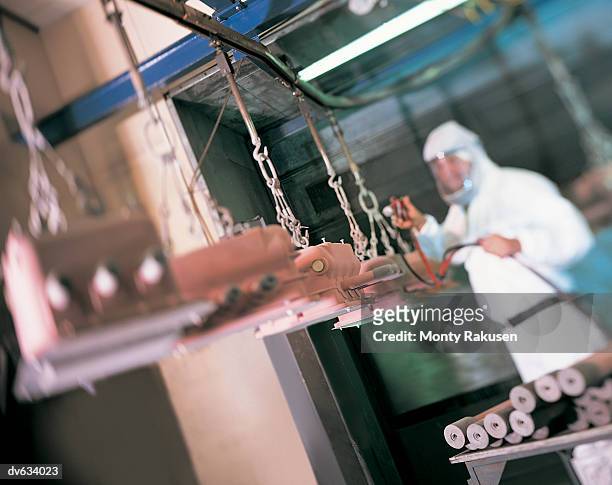 workman painting machine parts in spray booth - monty rakusen stock-fotos und bilder