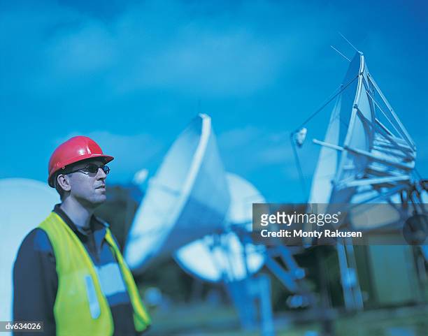 workman standing in front of array of radio satellite dishes - monty rakusen stock-fotos und bilder
