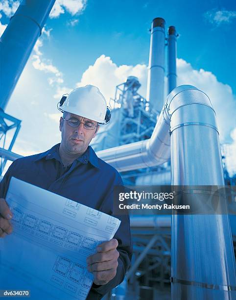 man reading blueprint in front of power station - monty rakusen stock pictures, royalty-free photos & images