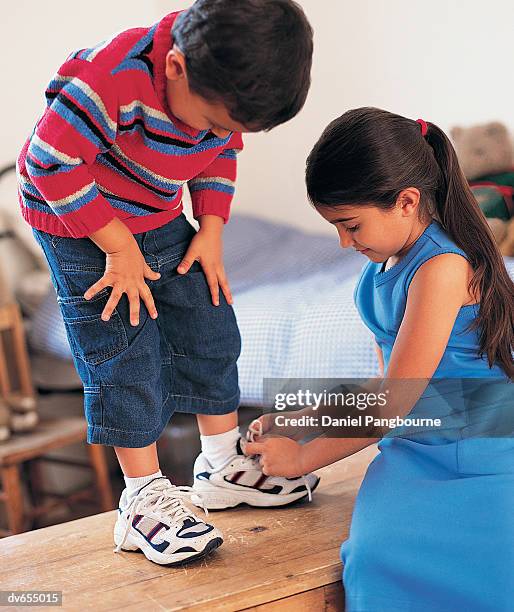 boy and his sister putting their shoes on - boy tying shoes stock-fotos und bilder