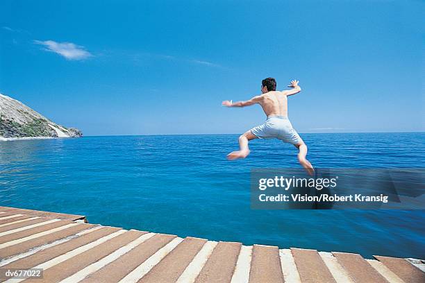 rear view of a young man in swimming trunks jumping into the sea from a pier - travel6 stock-fotos und bilder