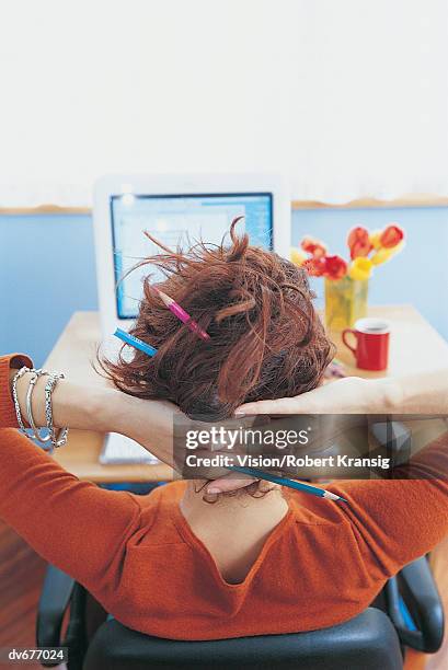 rear view of a businesswoman sitting at her desk with her hands behind her head and colouring pencils in her hair - colouring ストックフォトと画像