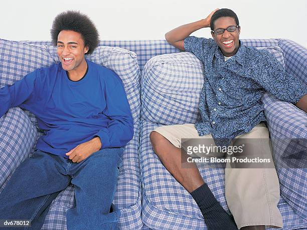 portrait of two men laughing on a sofa - tweezits bankje stockfoto's en -beelden