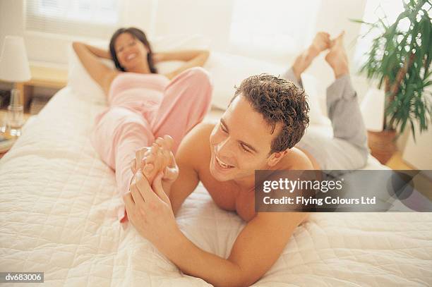 man giving a woman a foot massage in bed - woman lying on stomach with feet up stock pictures, royalty-free photos & images