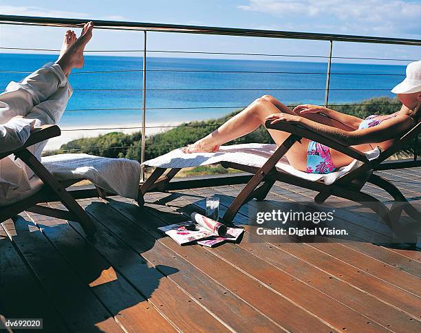 couple sunbathing on a balcony with the sea in the background - magazine retreat day 2 stock pictures, royalty-free photos & images