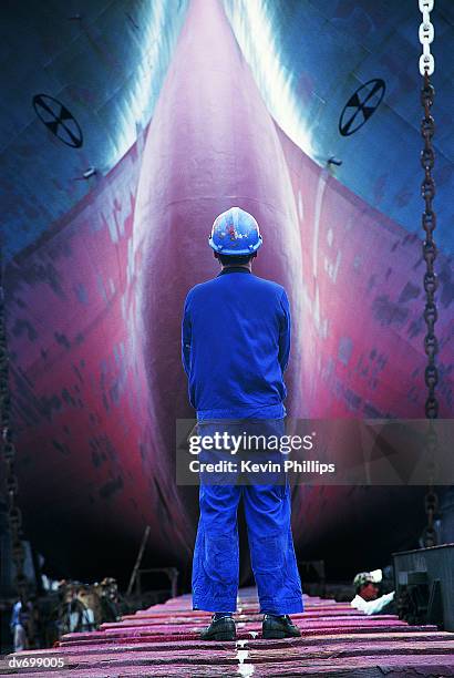rear view of shipyard worker standing in front of ship under construction, hong kong united dockyards, hong kong - 造船所 ストックフォトと画像