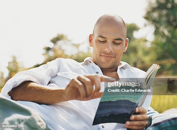 man reading a book in the park - libro in brossura foto e immagini stock
