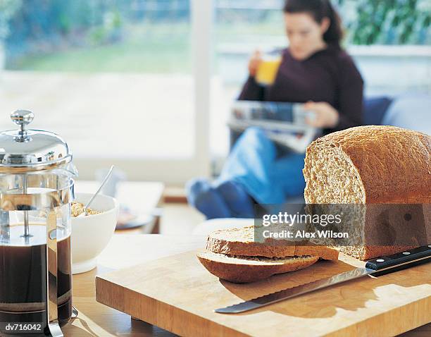 loaf of bread with a woman reading a newspaper in the background - loaf stock pictures, royalty-free photos & images