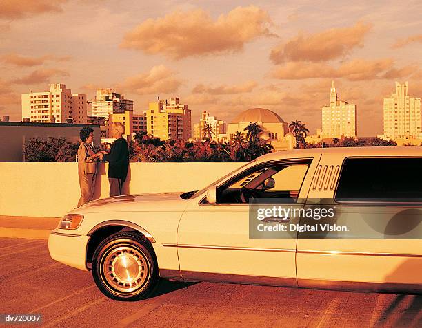 mature couple standing beside limousine in front of city skyline - limousine exterior stock pictures, royalty-free photos & images