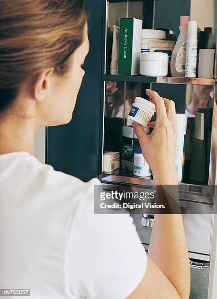 woman examining a bottle of medicine - armoire de toilette photos et images de collection
