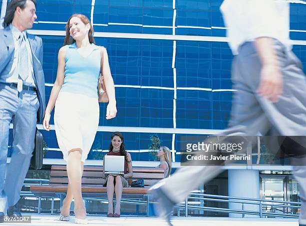 distant portrait of a young businesswoman sitting on a bench and business people walking by - distant imagens e fotografias de stock
