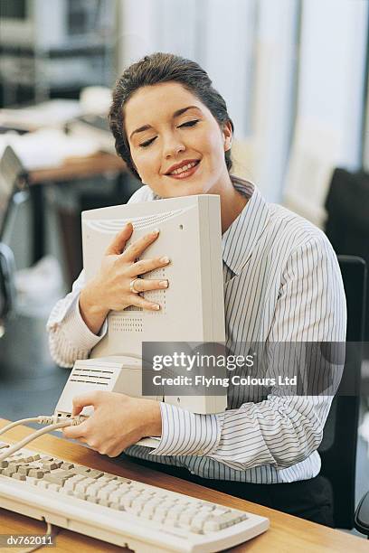 businesswoman cuddling her computer monitor at her desk - technophiler mensch stock-fotos und bilder