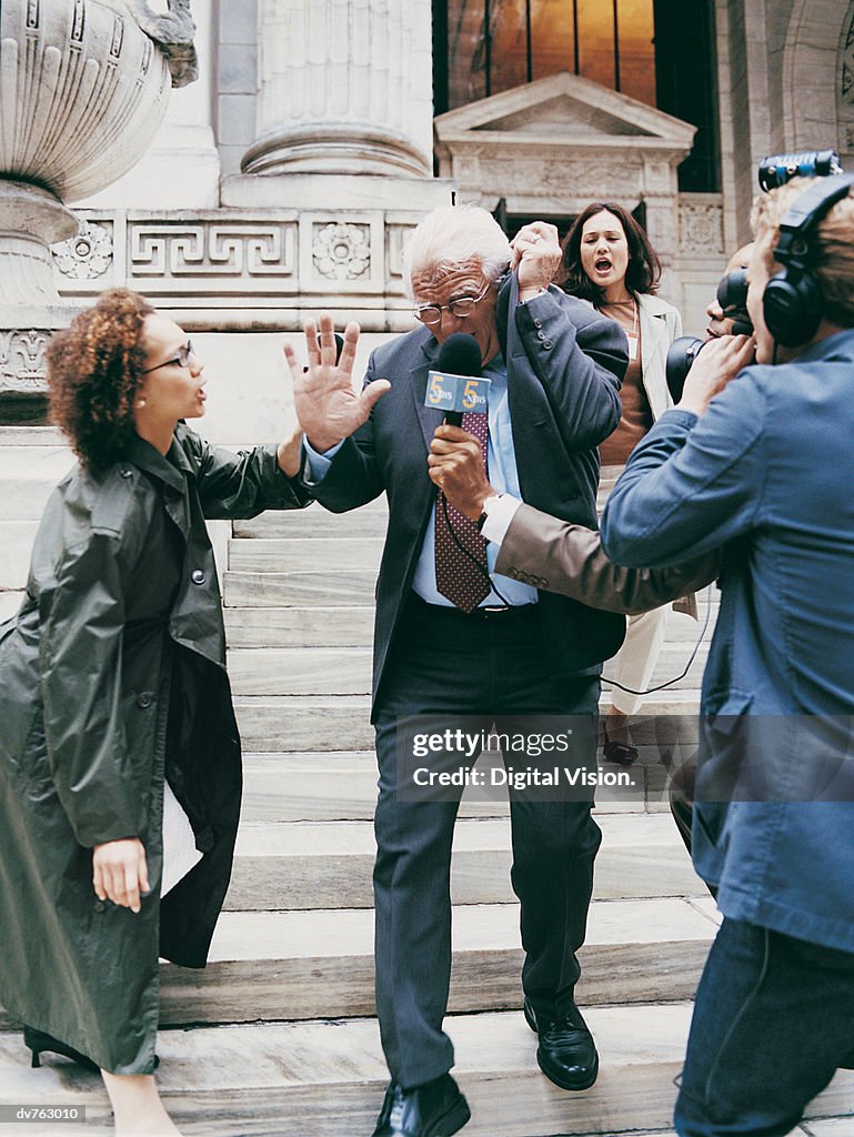News Reporters Trying to Interview a Mature Man in a Suit on the Steps of a Building