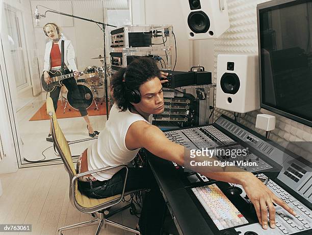 producer adjusting a sound mixer as a pop musician plays a guitar in a recording studio - roupa de discoteca imagens e fotografias de stock