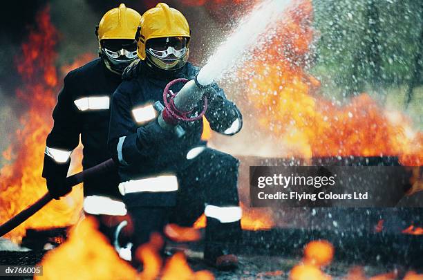 firefighters holding a hose and spraying water - brandslang stockfoto's en -beelden