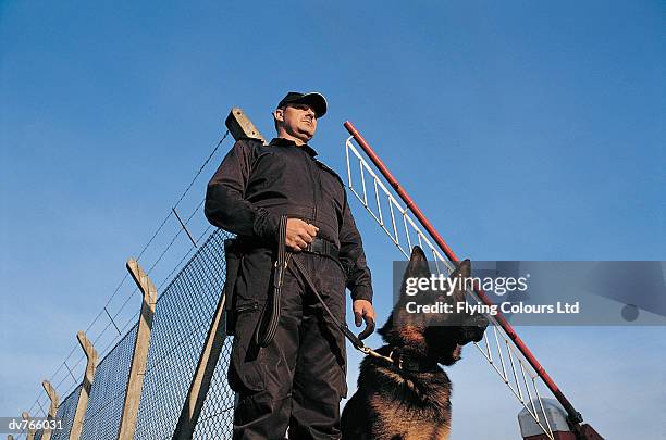 security guard with a guard dog standing in front of security barrier and chainlink fence - barrier imagens e fotografias de stock