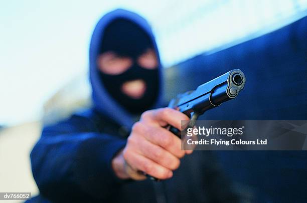 male criminal wearing a baraclava and aiming a gun - thief stock pictures, royalty-free photos & images