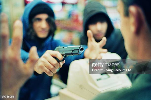 hooded criminals threatening a shop assistant with a gun - gun shop - fotografias e filmes do acervo