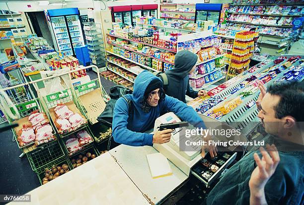 high angle view of two robbers robbing a cash till and threatening a shop assistant with a gun - stealing crime ストックフォトと画像