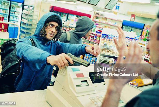 two robbers threatening a shop assistant with a gun - gun shop - fotografias e filmes do acervo