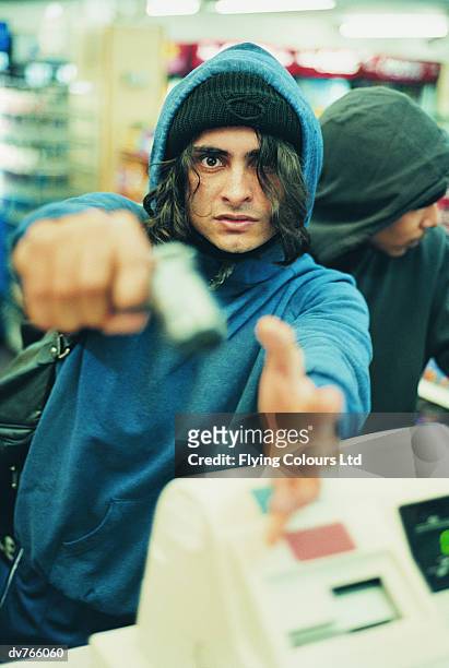 portrait of a hooded robber with another man aiming a pistol - stranger danger stock pictures, royalty-free photos & images