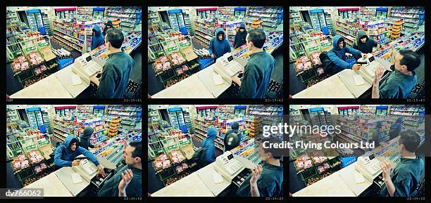 high angle view of two robbers robbing a cash till and threatening a shop assistant with a gun - stehlen verbrechen stock-fotos und bilder